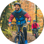 Thumbnail Image showing an exterior photograph of a young man and friend biking in the woods on a trail